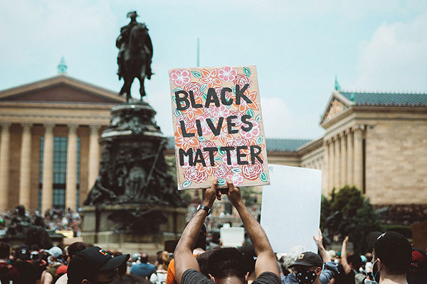 BLM protestor holds sign. [Text reads: Higher Education Faculty.]